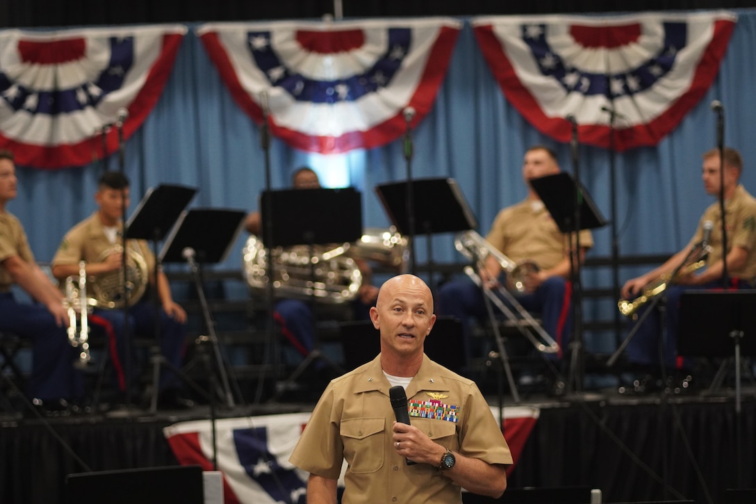 A Marine Corps General speaks in front of a Marine Corps Band during an event at a school
