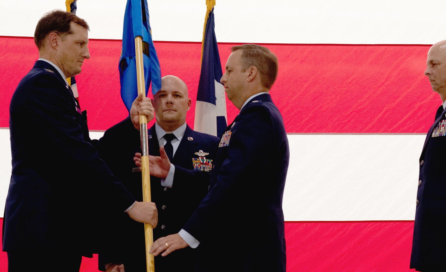Man in Air Force uniforms hands flag to another man in Air Force uniform while on stage.