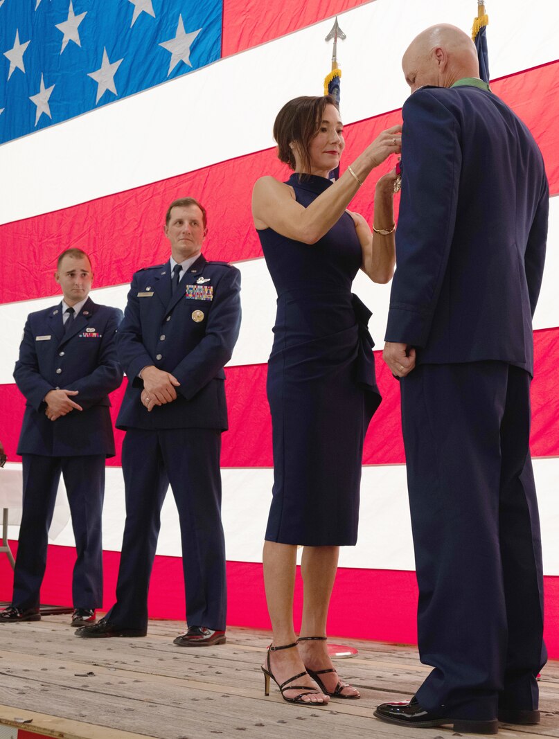 woman places lapel pin on man in Air Force uniform while on stage.