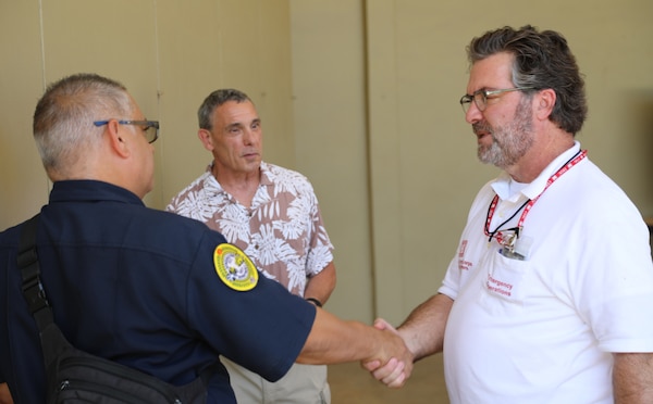 Two men shake hands with another man