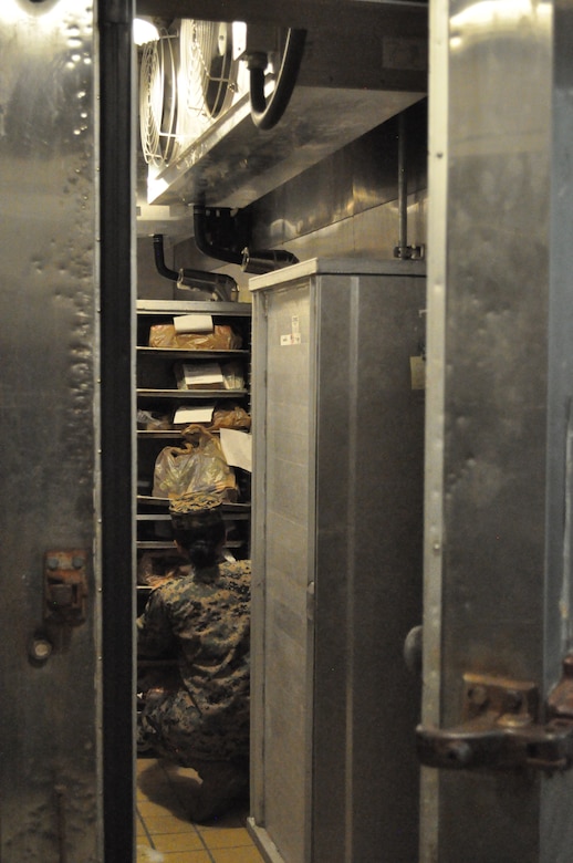 A Marine searches for frozen items in a mess hall freezer.