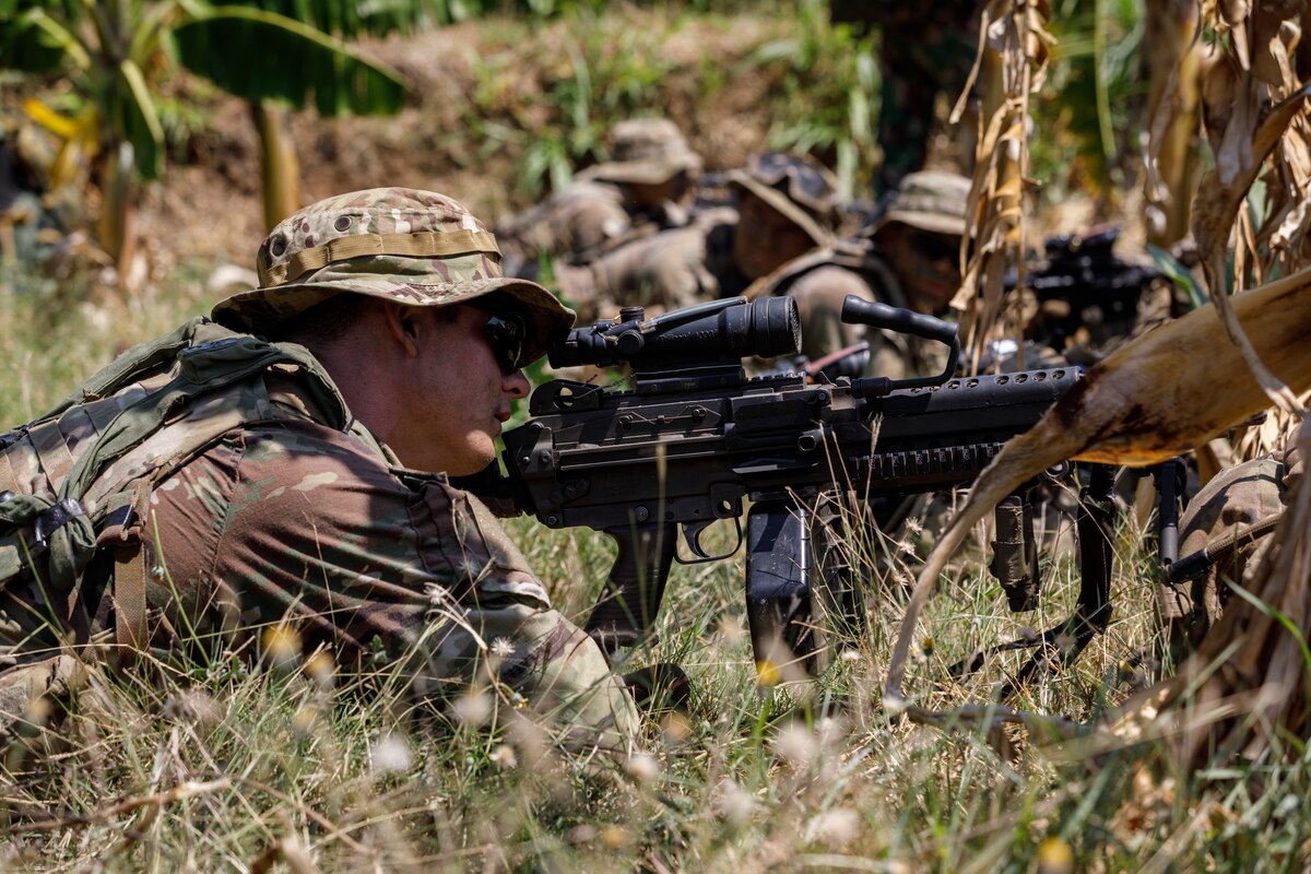A soldier lies on the ground looking through the scope of a weapon.