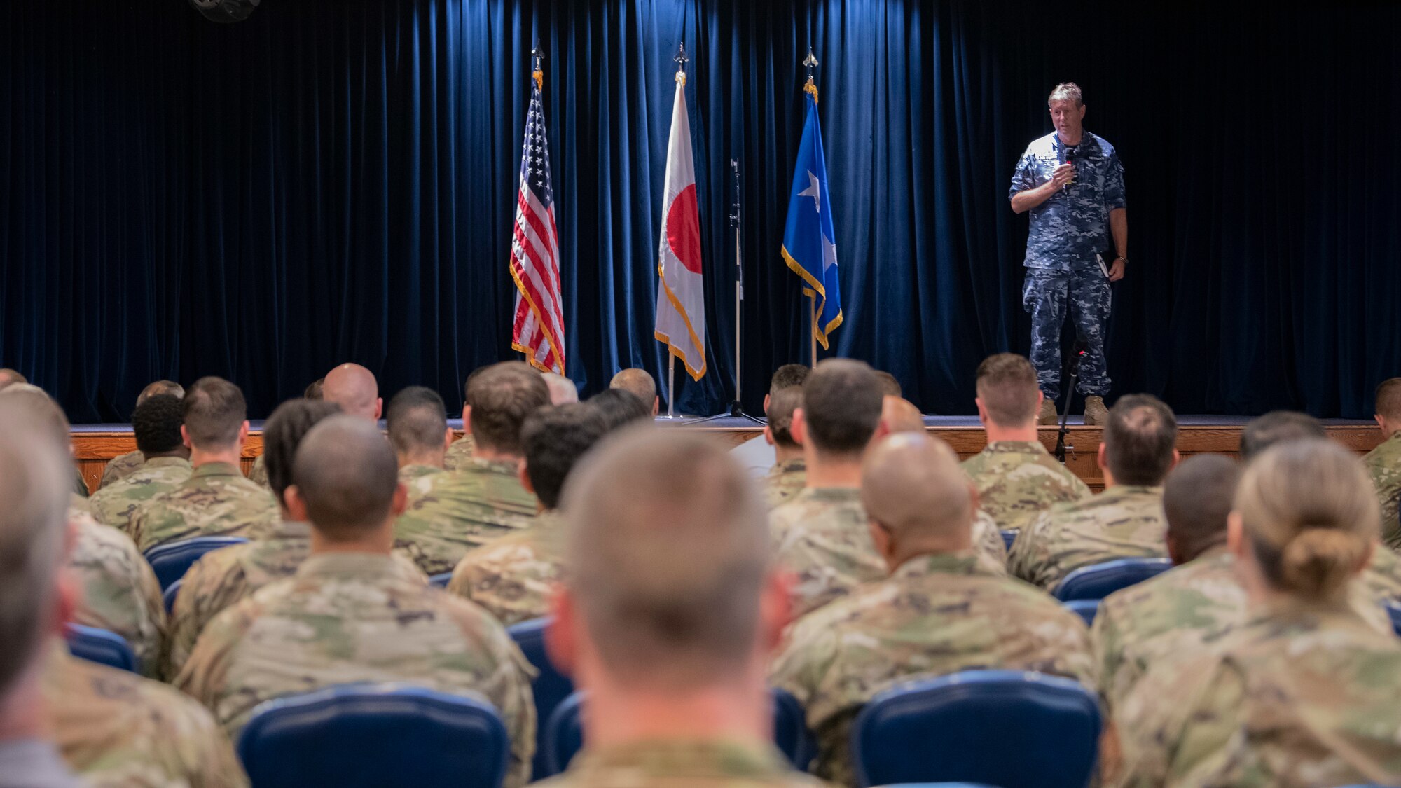 A military man on a stage speaks to a crowd.