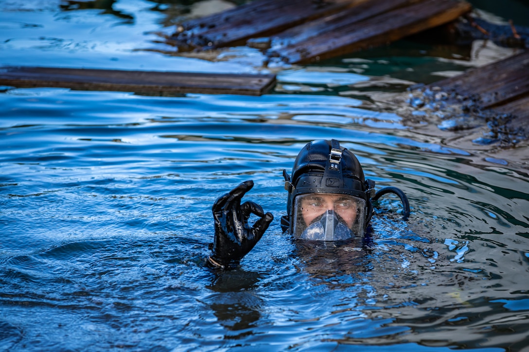 A sailor  in diving gear signals from the water.