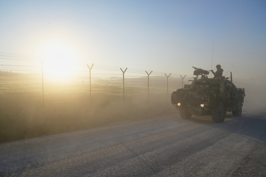 A soldier rides in a tank down a road at sunset.