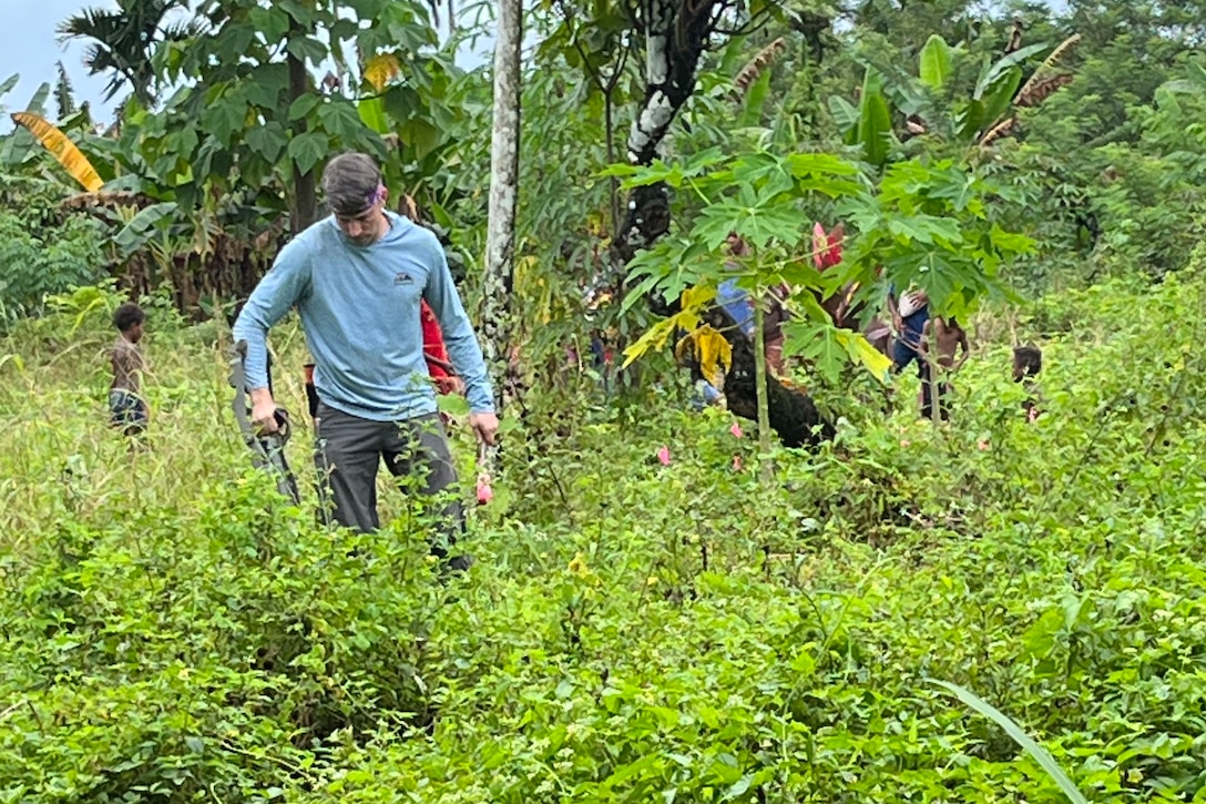 A soldier searches through a forested area.