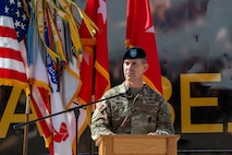 A male soldier stand behind a podium outside.