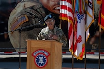 A female Army soldier stands behind a podium outside.