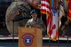 A female Army soldier stands behind a podium outside.