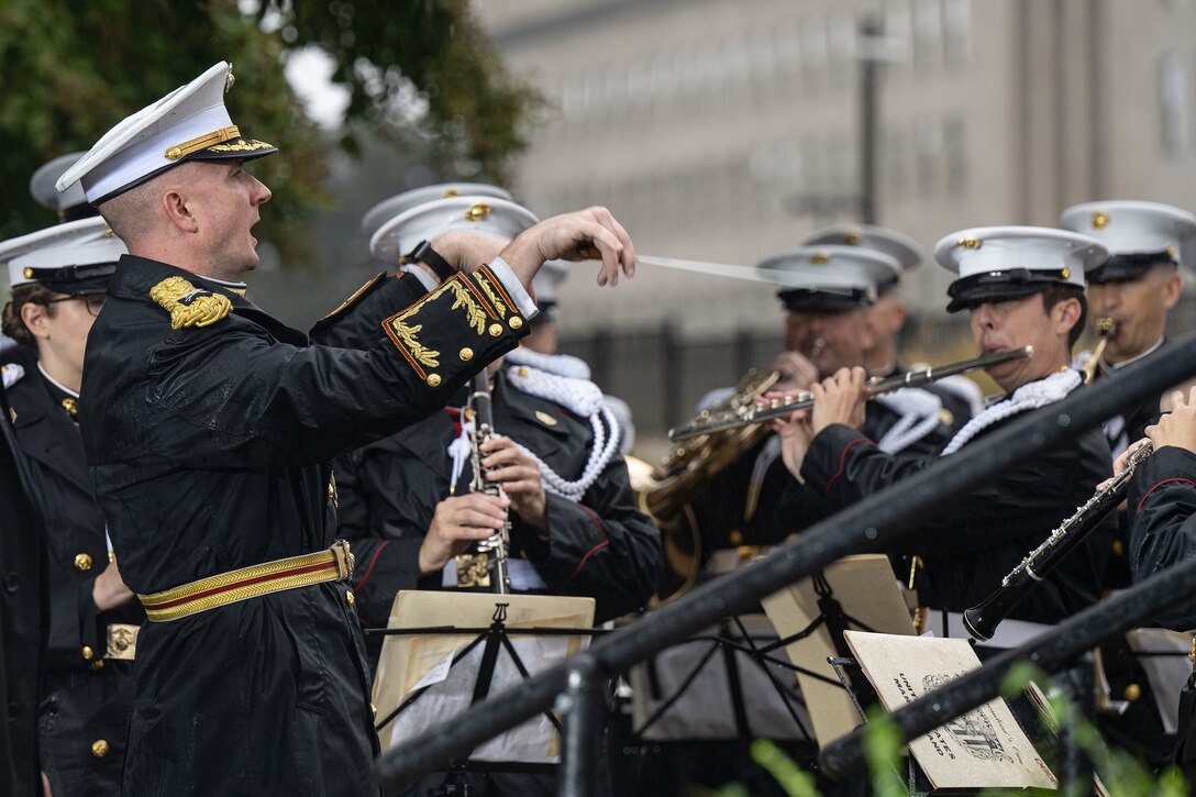 Marine musicians play music outside the Pentagon as a conductor gestures with a baton.