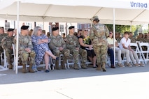 Group of soldiers and civilians sit under a tent outside.