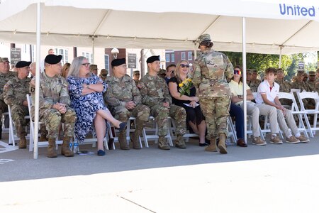 Group of soldiers and civilians sit under a tent outside.