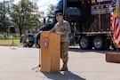 A man in US Army uniform stands behind a podium outside.