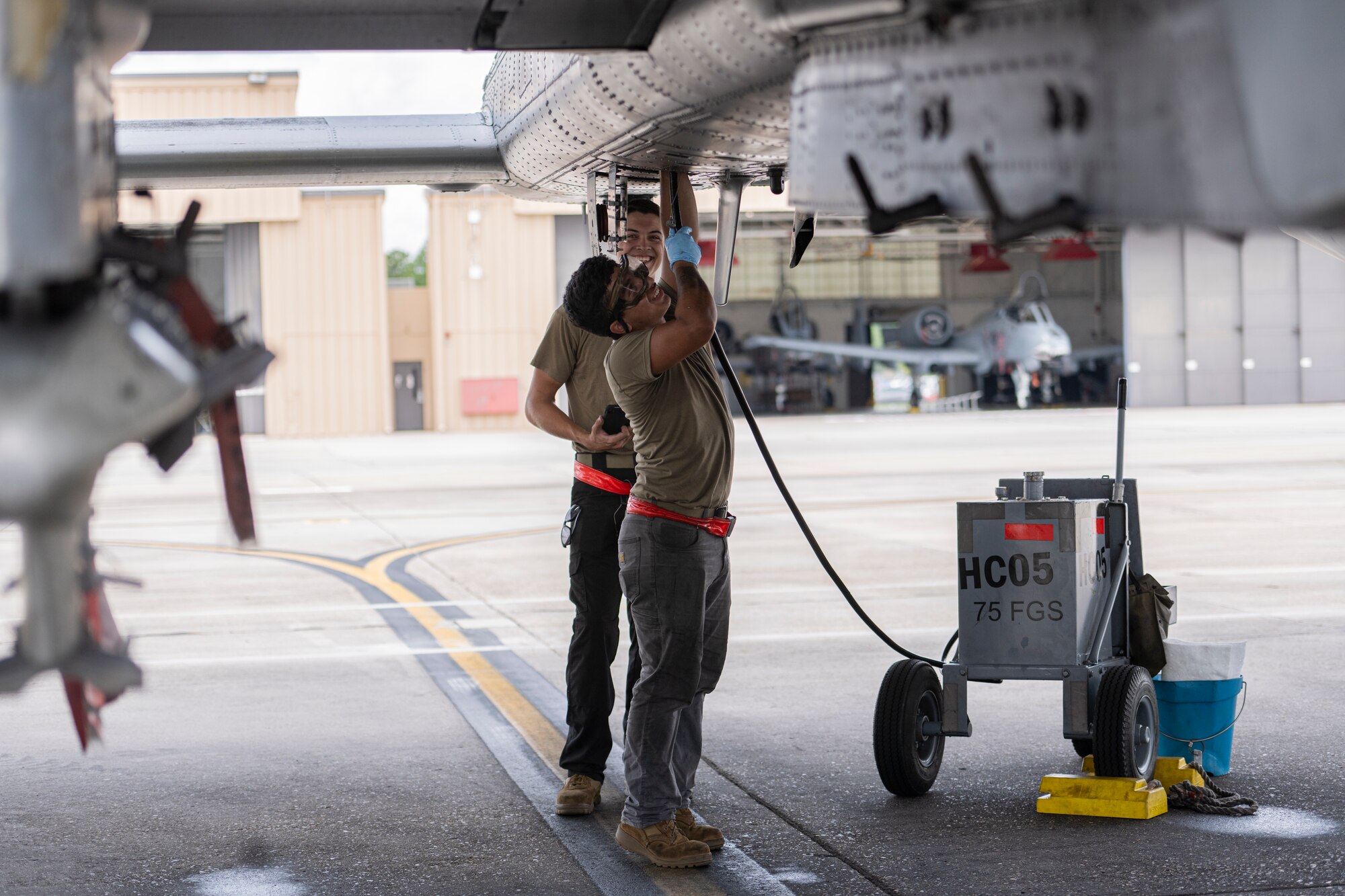 Two Airman connect a hose to the bottom of an aircraft