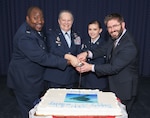 Two men and two women stand in front of a large cake with a sword.