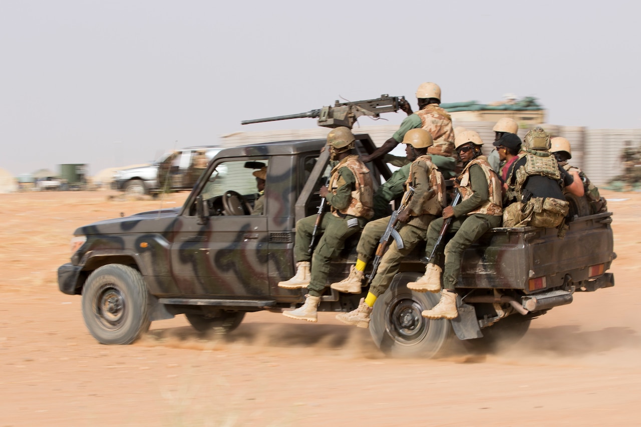 Foreign troops ride in the bed of a military pickup truck.