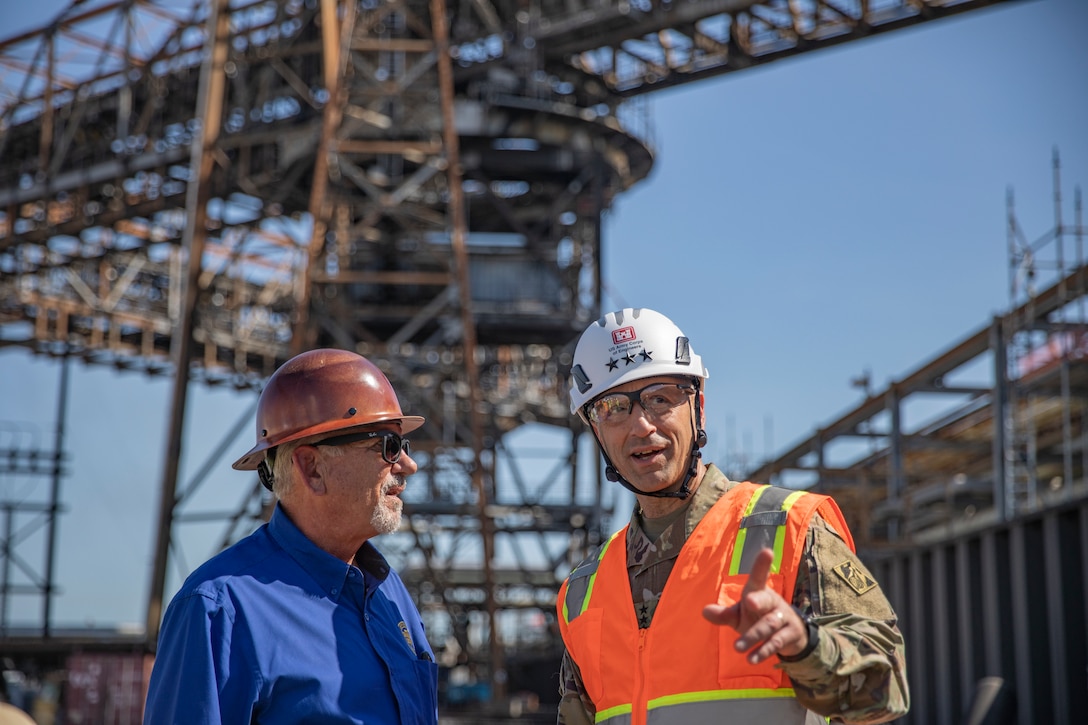 people in hard hats and safety vests are standing in an oil refinery, talking.