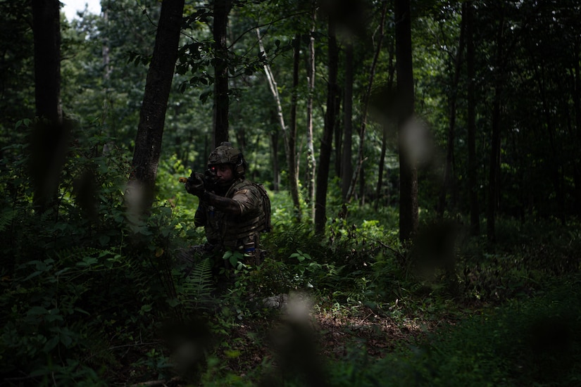 An airman walks through a wooded area.