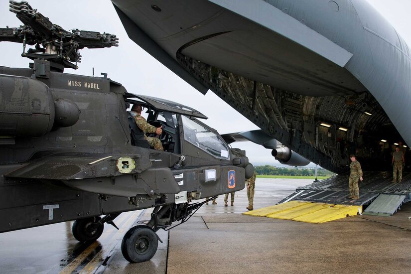 Soldiers prepare to load a helicopter onto a parked aircraft.