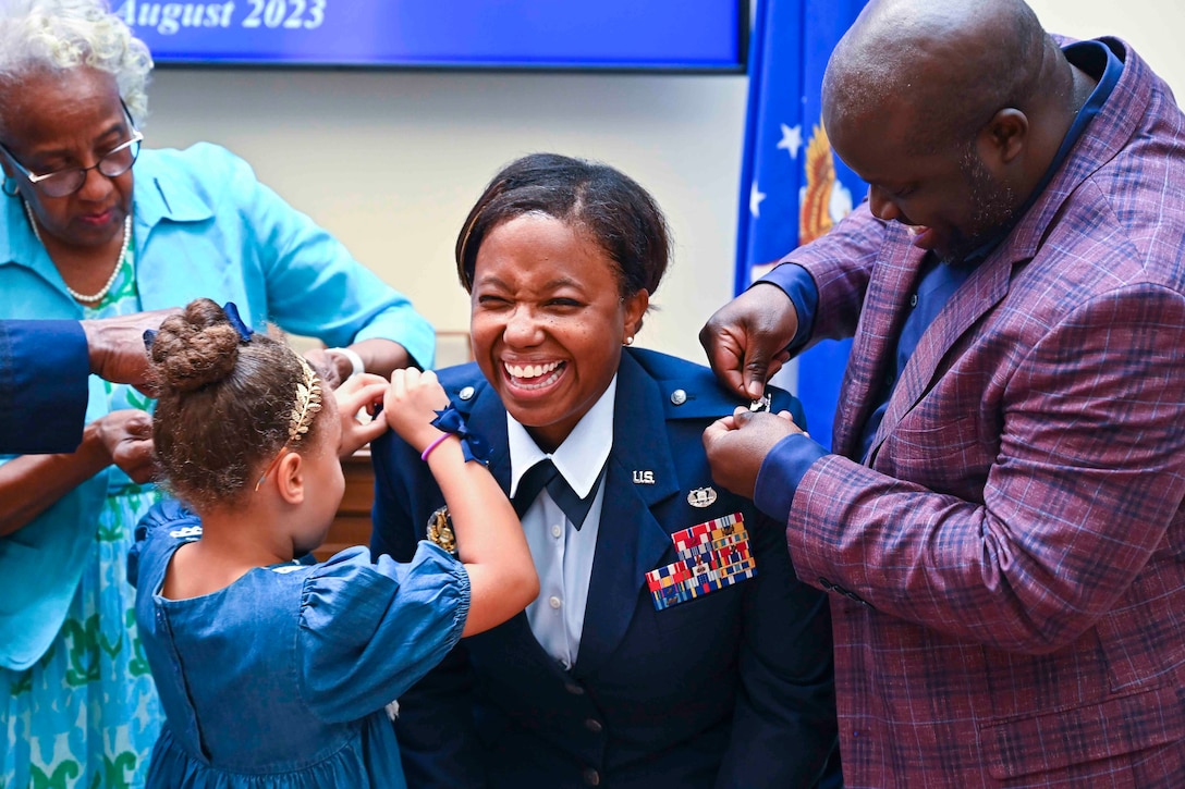 An airman smiles as a woman, a child and a man place pins on her uniform.