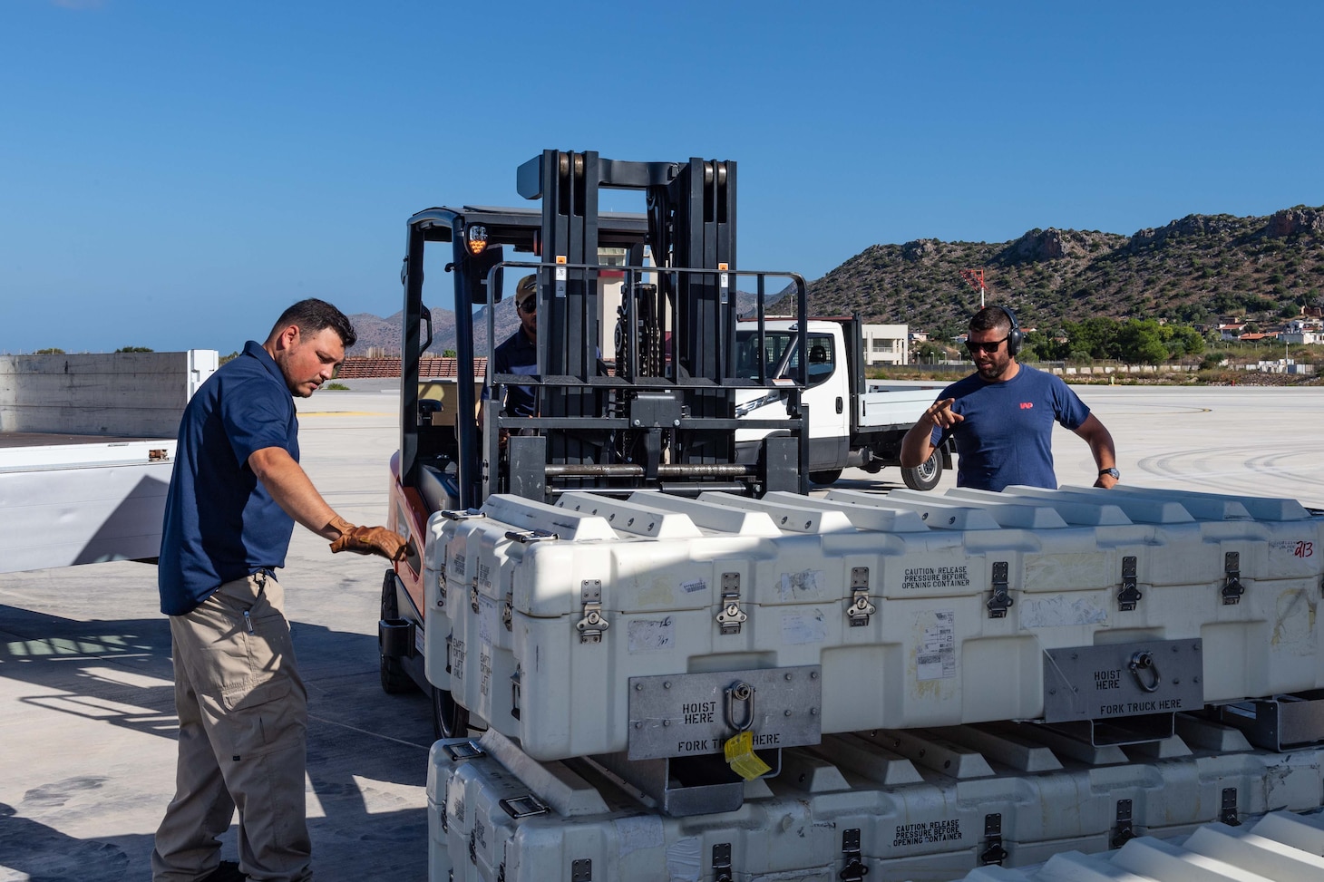 Logistics Specialist 1st Class Sebastian Martin (left), assigned to the Supply Department of USS Gerald R. Ford (CVN 78), and Kanakis Pantelakis, a shipping and receiving contractor working at Naval Support Activity Souda Bay Air Cargo Services department, load cargo destined for the ship onto a forklift operated by Logistics Specialist 2nd Class Dametri Allen, Supply Department of Gerald R. Ford, Aug. 31, 2023.