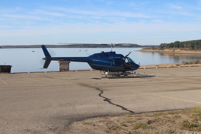 A helicopter sits on a slab of concrete with a lake and blue sky in the background.