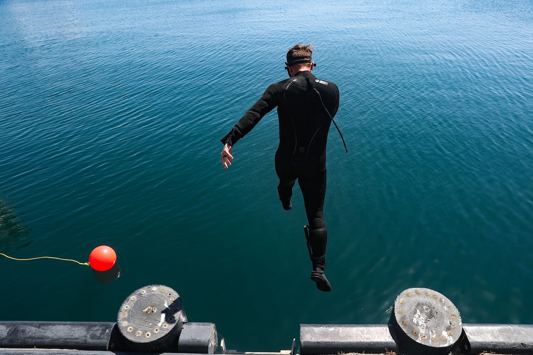 A sailor in a wetsuit jumps into water.