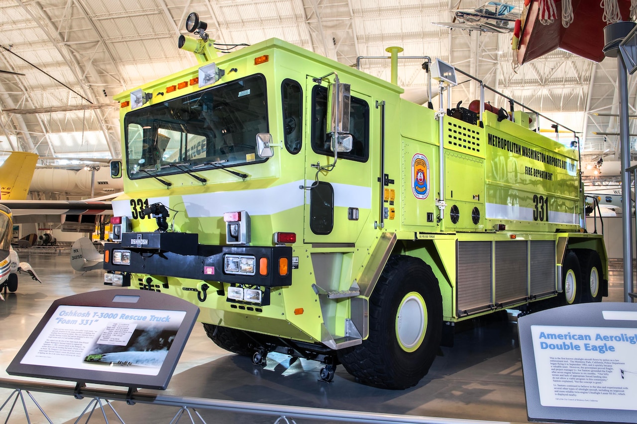 A fire rescue truck sits on display in a large hangar.