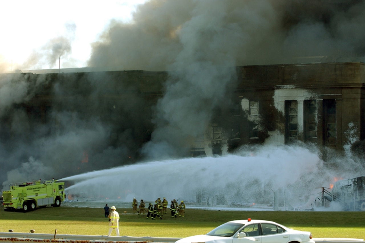 A fire rescue vehicle sprays fire-suppressant foam onto a large, damaged building.