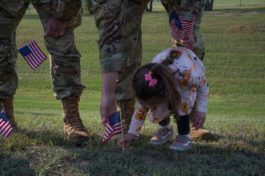 U.S. Air Force Staff Sgt. Richard Arias helps his daughter plant a flag at Minot Air Force Base, North Dakota, Sept. 6, 2023. The Airman volunteered for the third annual flag planting for Suicide Prevention Month. (U.S. Air Force photo by Airman 1st Class Trust Tate)