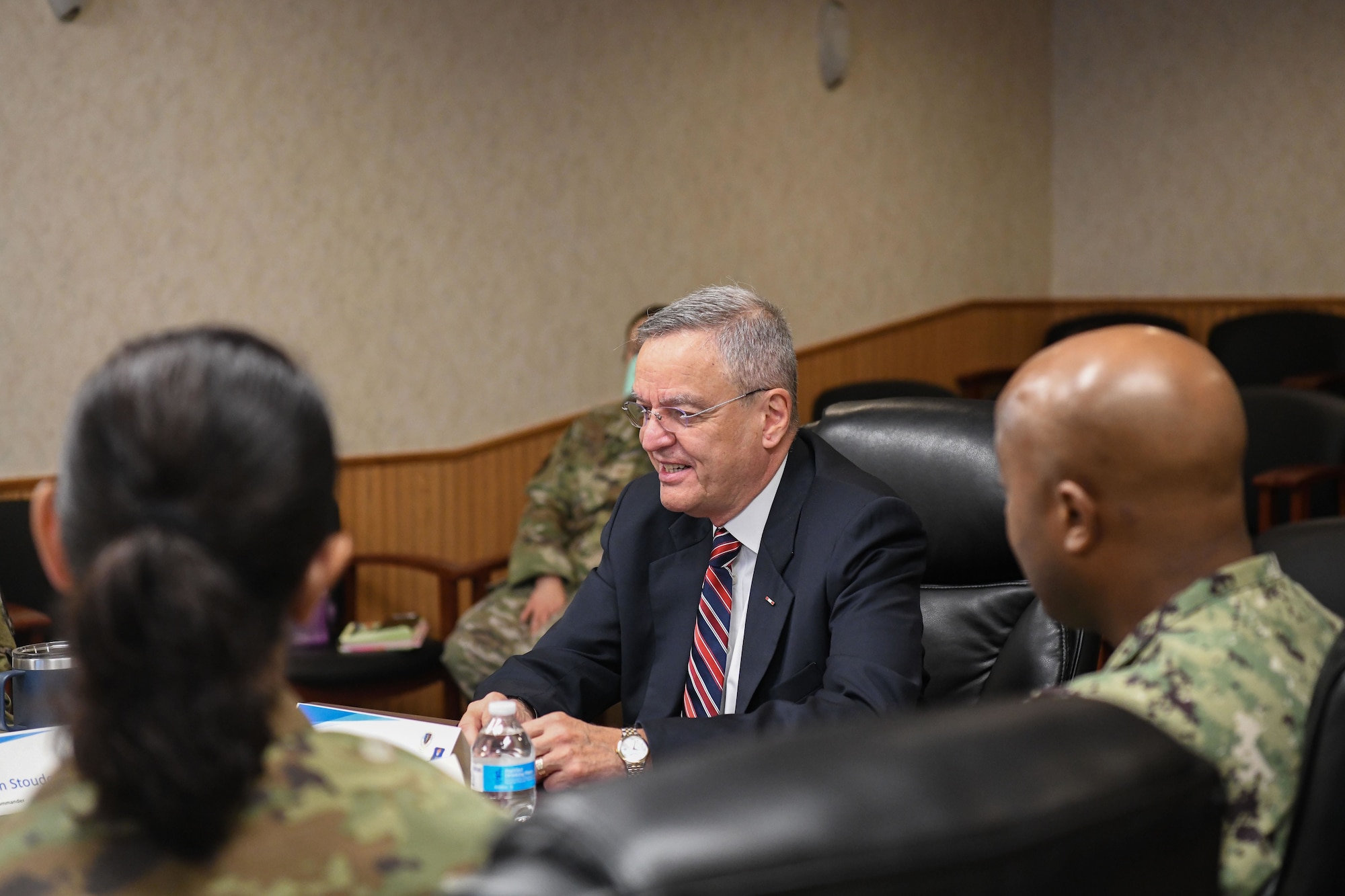 Man in suits sits at a table with military members.
