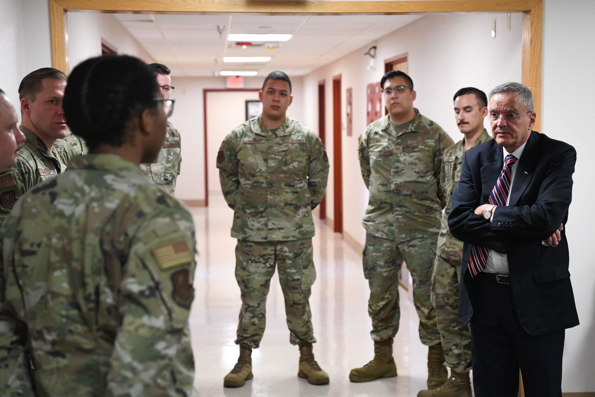Man in suits talks to uniformed service members.