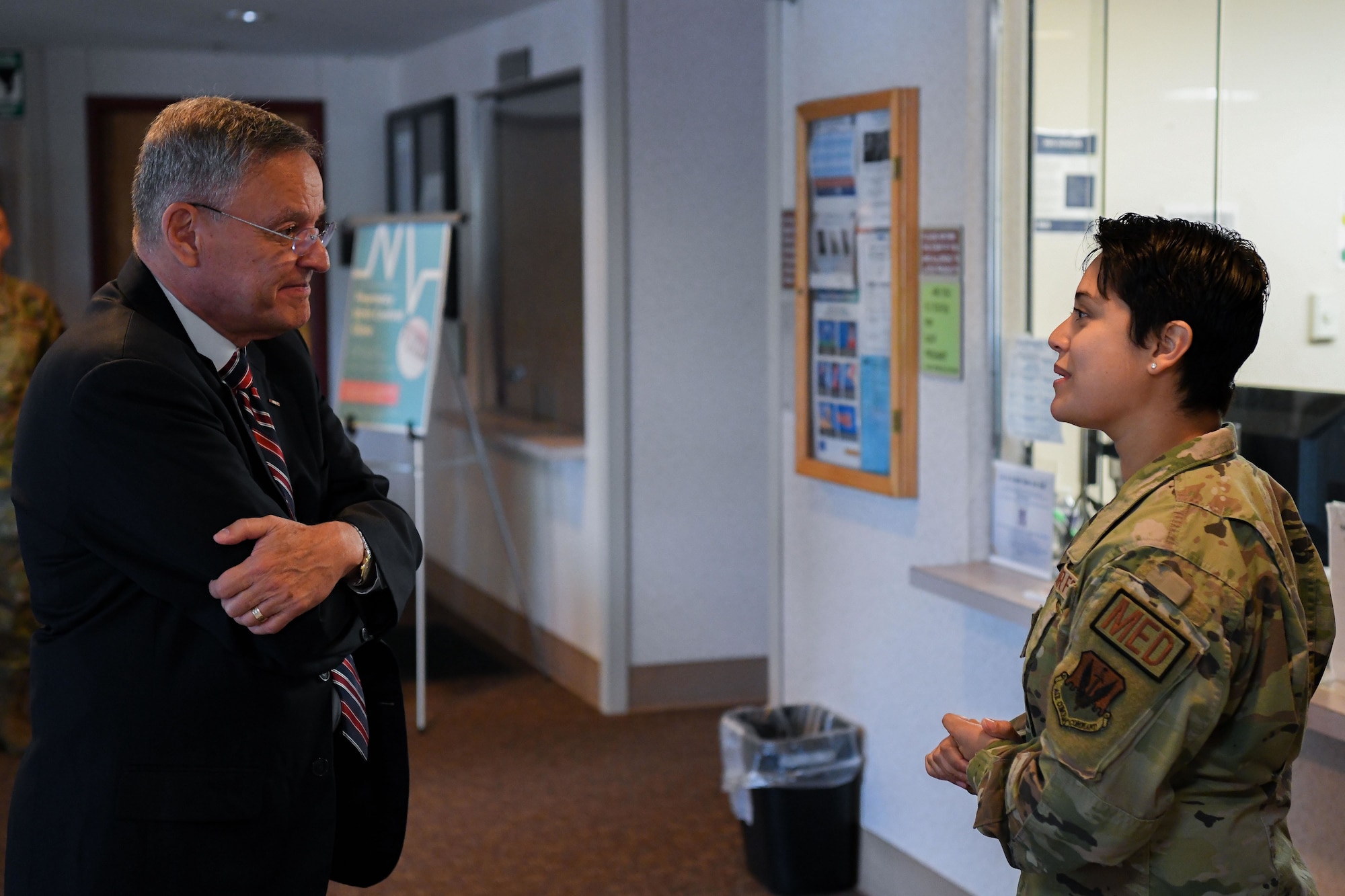 A man in a suit talks to a woman in a military uniform.