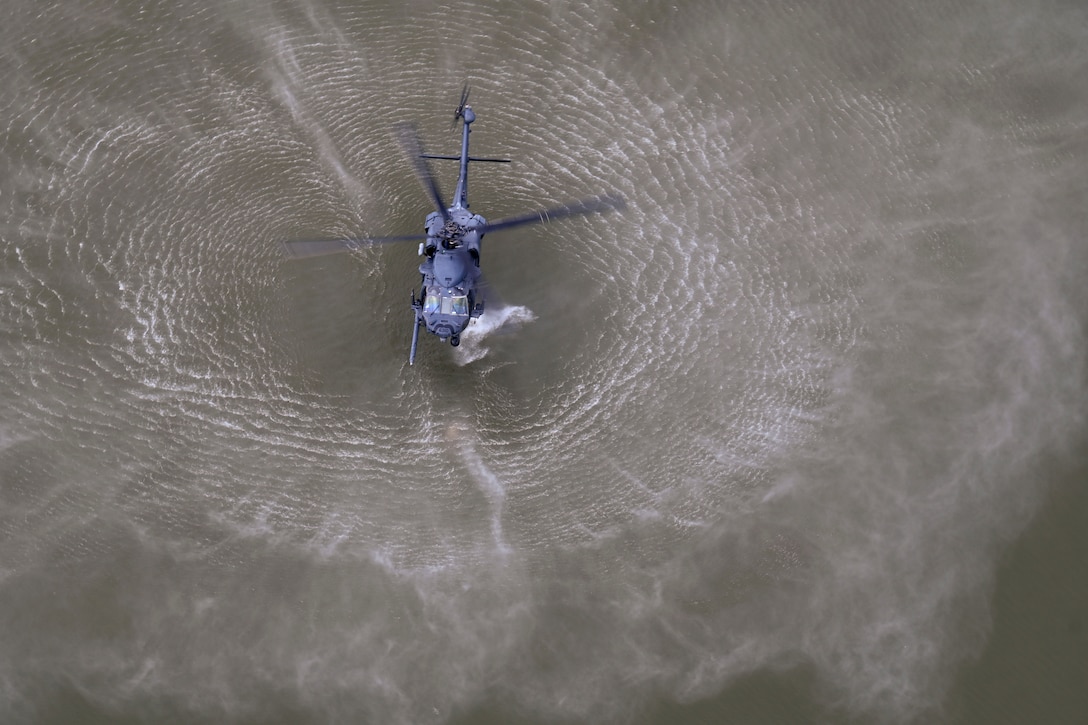 A helicopter creates ripples as it hovers over a body of water as seen from above.