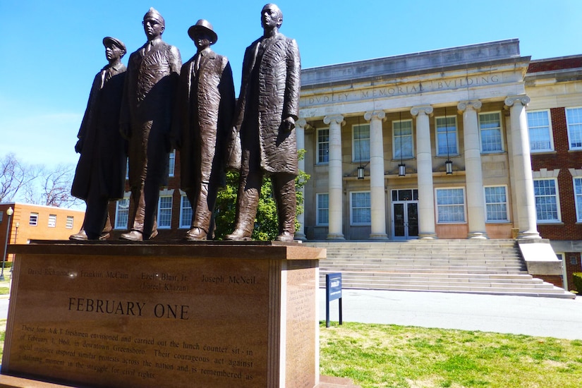 Statue depicting four people in front of a university building.