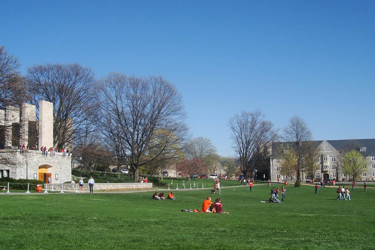 A university campus is photographed during daylight hours with people seated on grass.