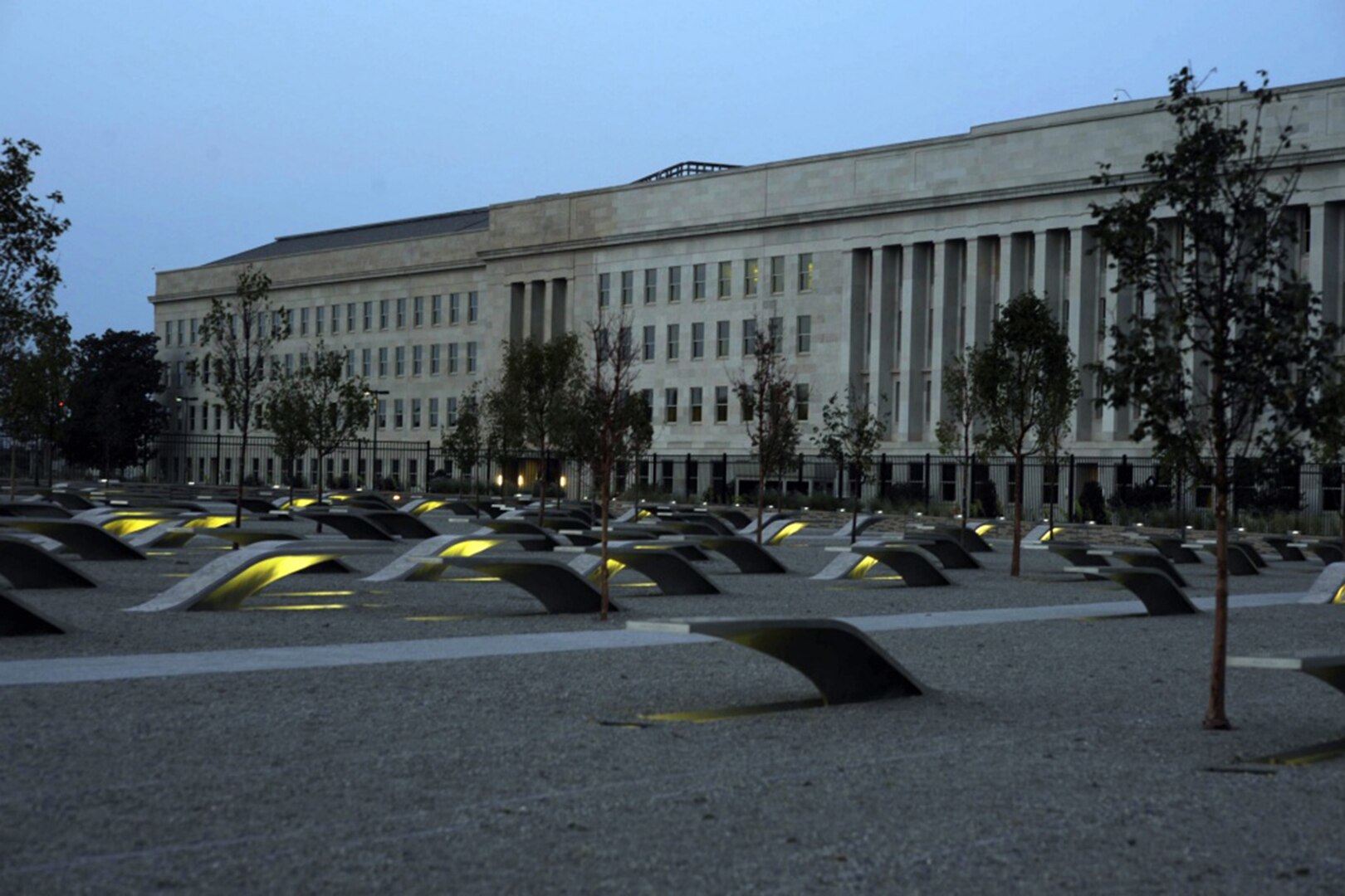 Dozens of small, curved structures rise from the ground in front of a large building.