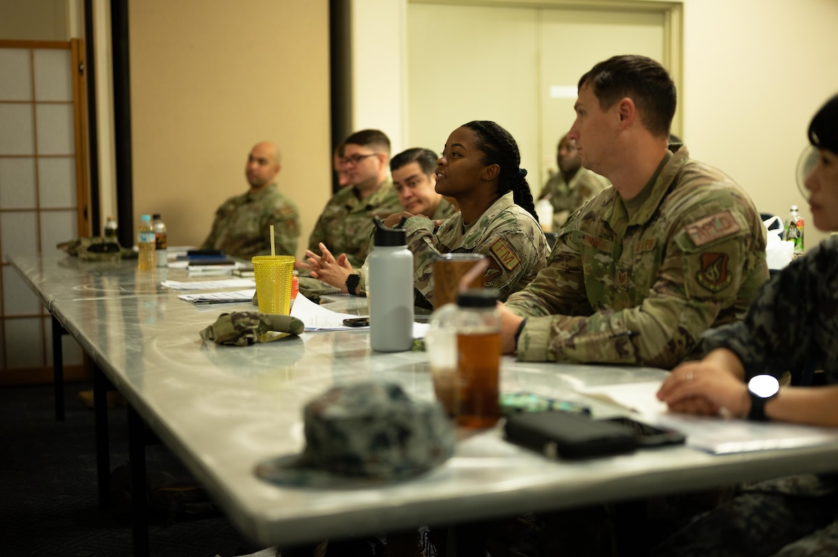 A line of Air Force and JASDF members sit at a table and participate in a SNCO Professional Enhancement Seminar.
