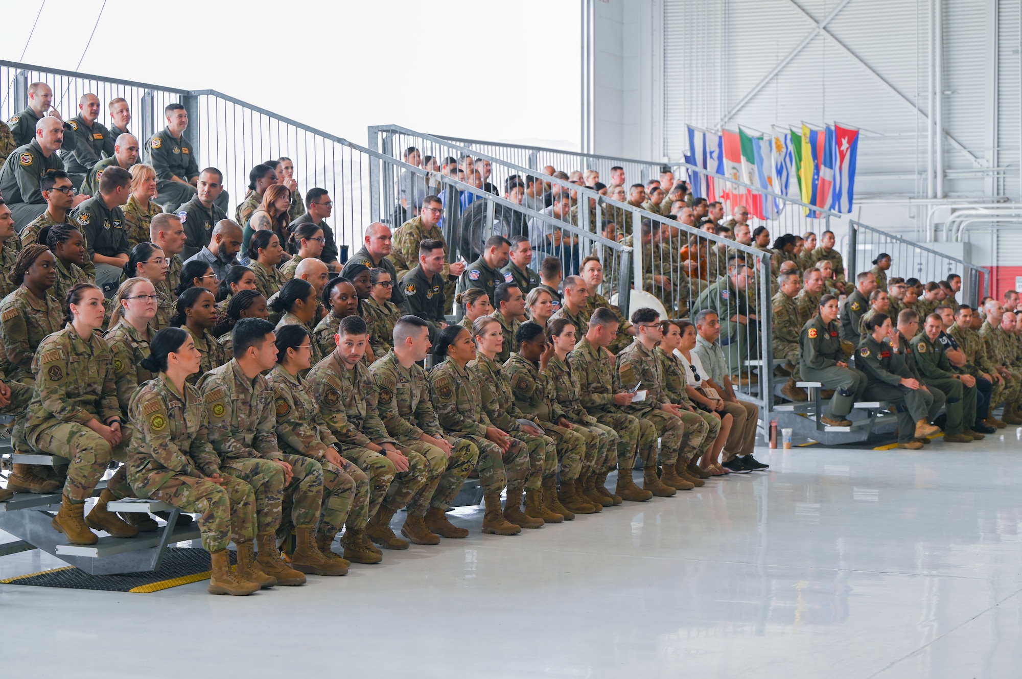 Airmen dressed in uniforms sit on two sets of bleachers waiting for the ceremony to begin