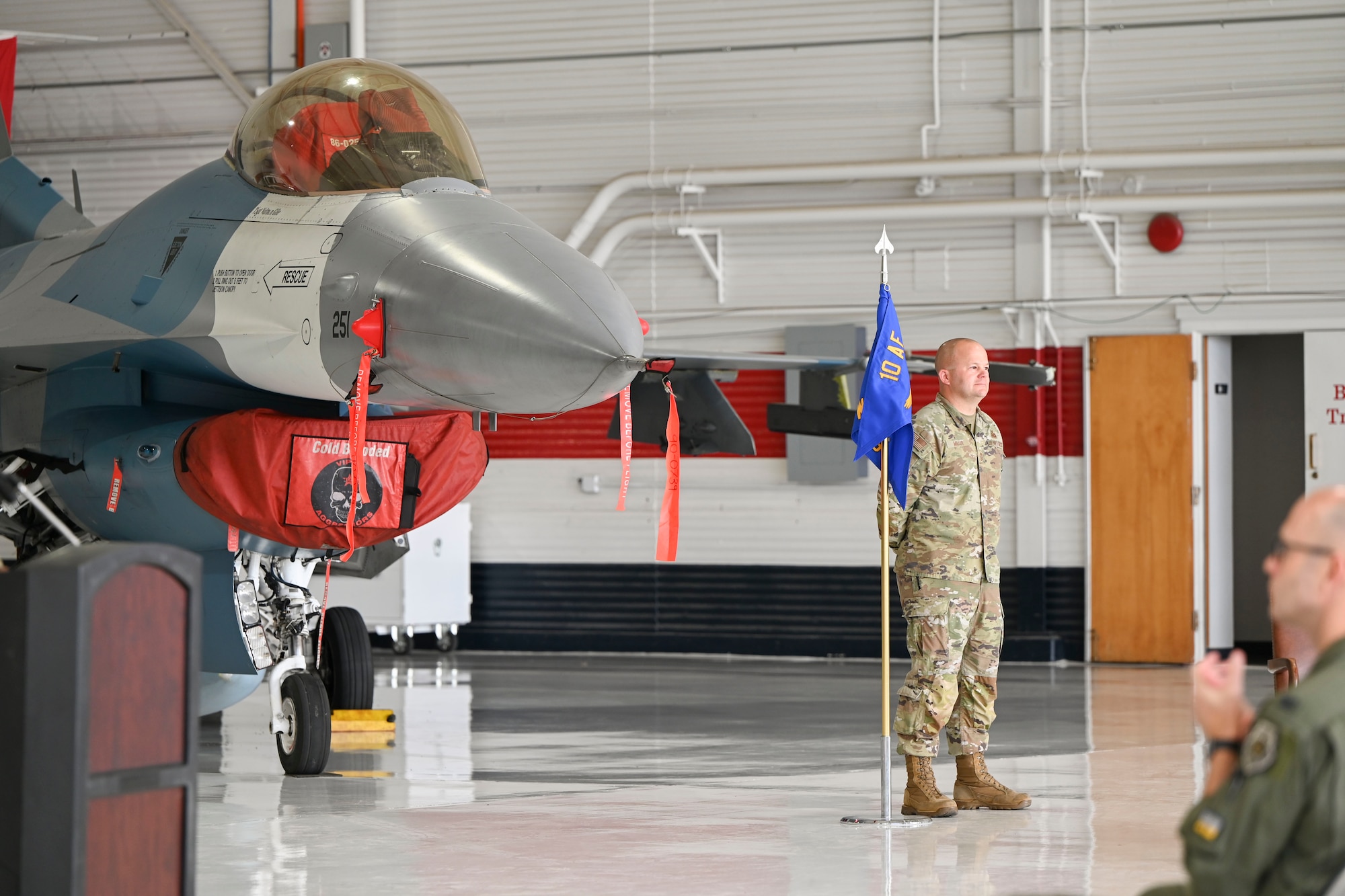 An airman holds a flag during a ceremony where an F-16 Falcon is the backdrop.