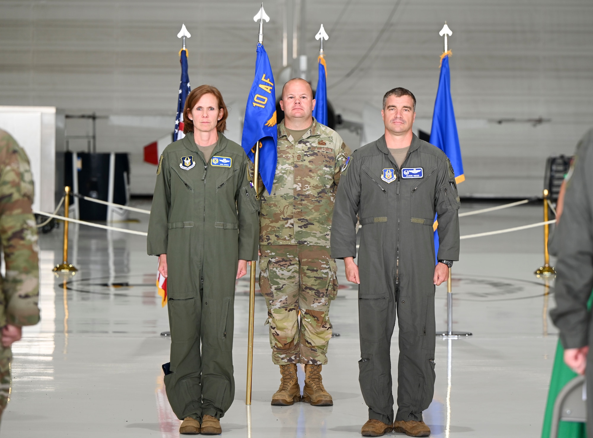 Three military members stand near the guidon and look towards the crowd during a ceremony