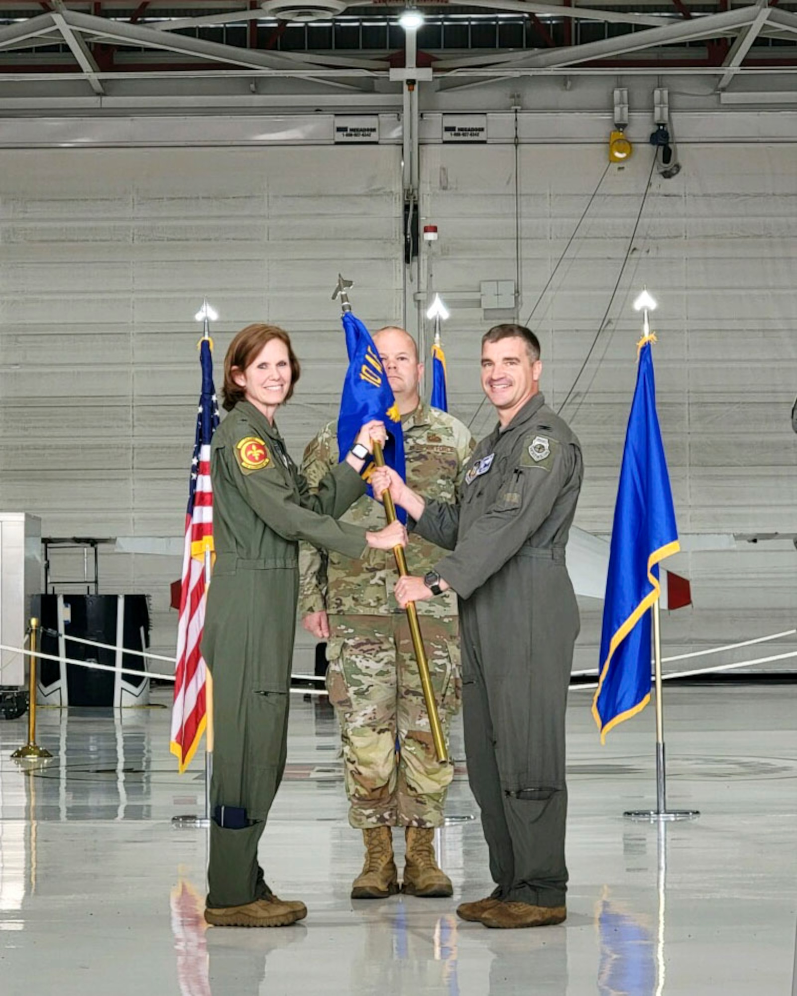 Two military members wearing flight suits look towards the camera as they hold a flag.