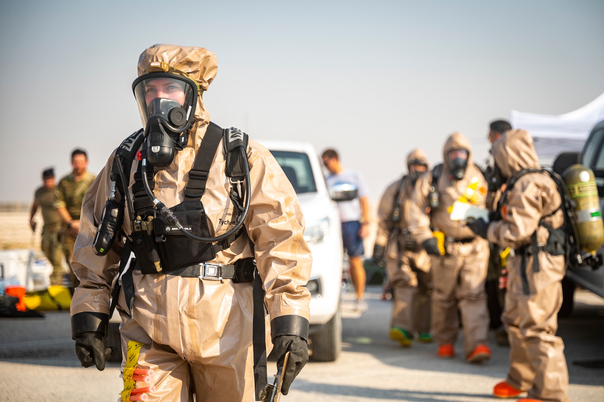 Military member in chemical gear begins walking towards the front entrance of a building.