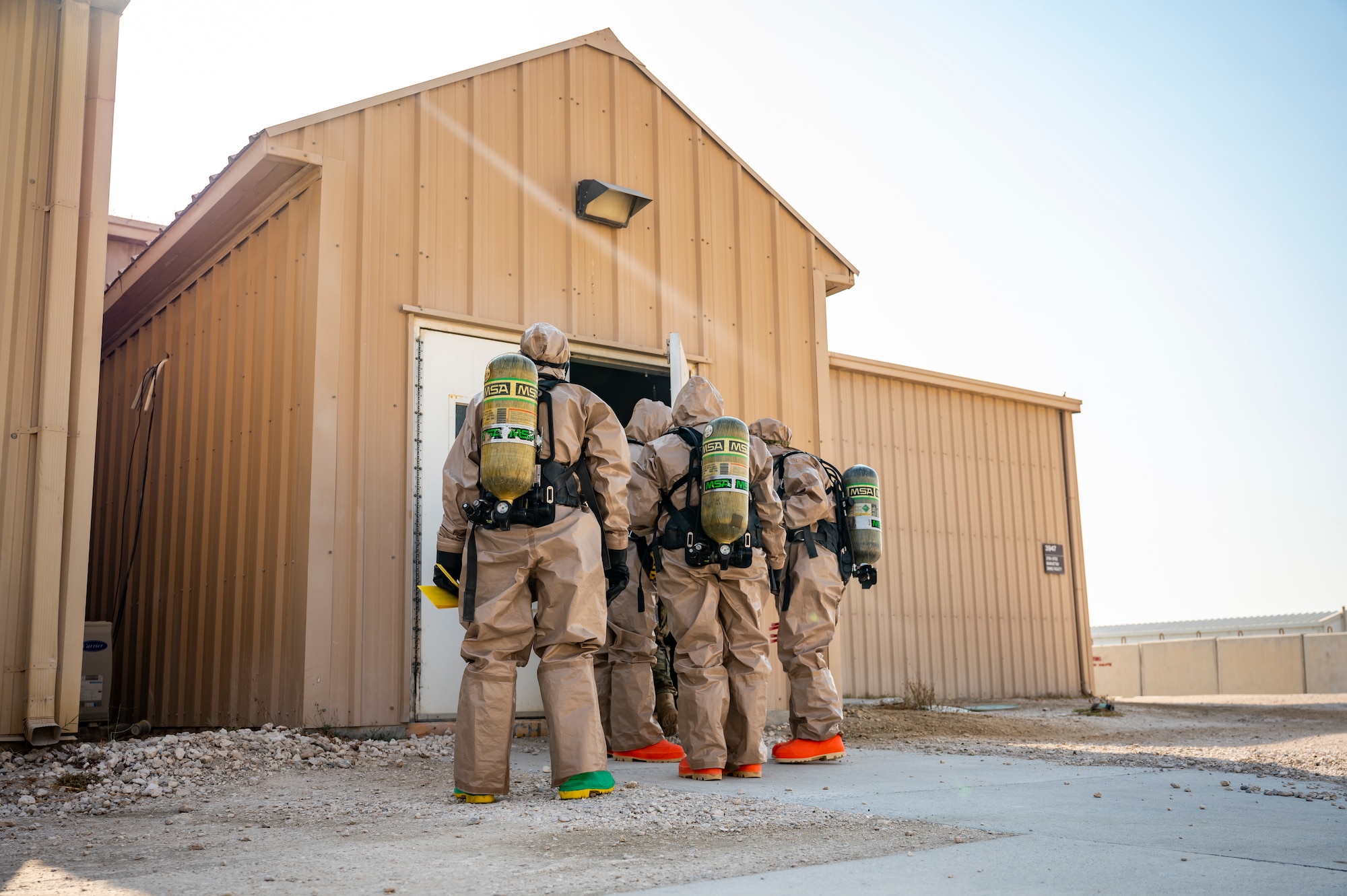 Military members in chemical gear prepare to walk through the front entrance of a building