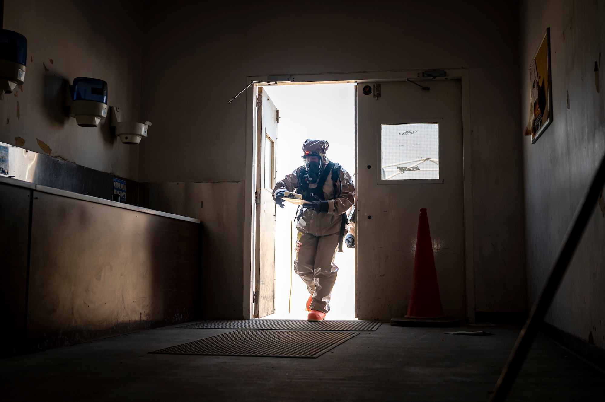 Military member in chemical gear walks through the front entrance of a building