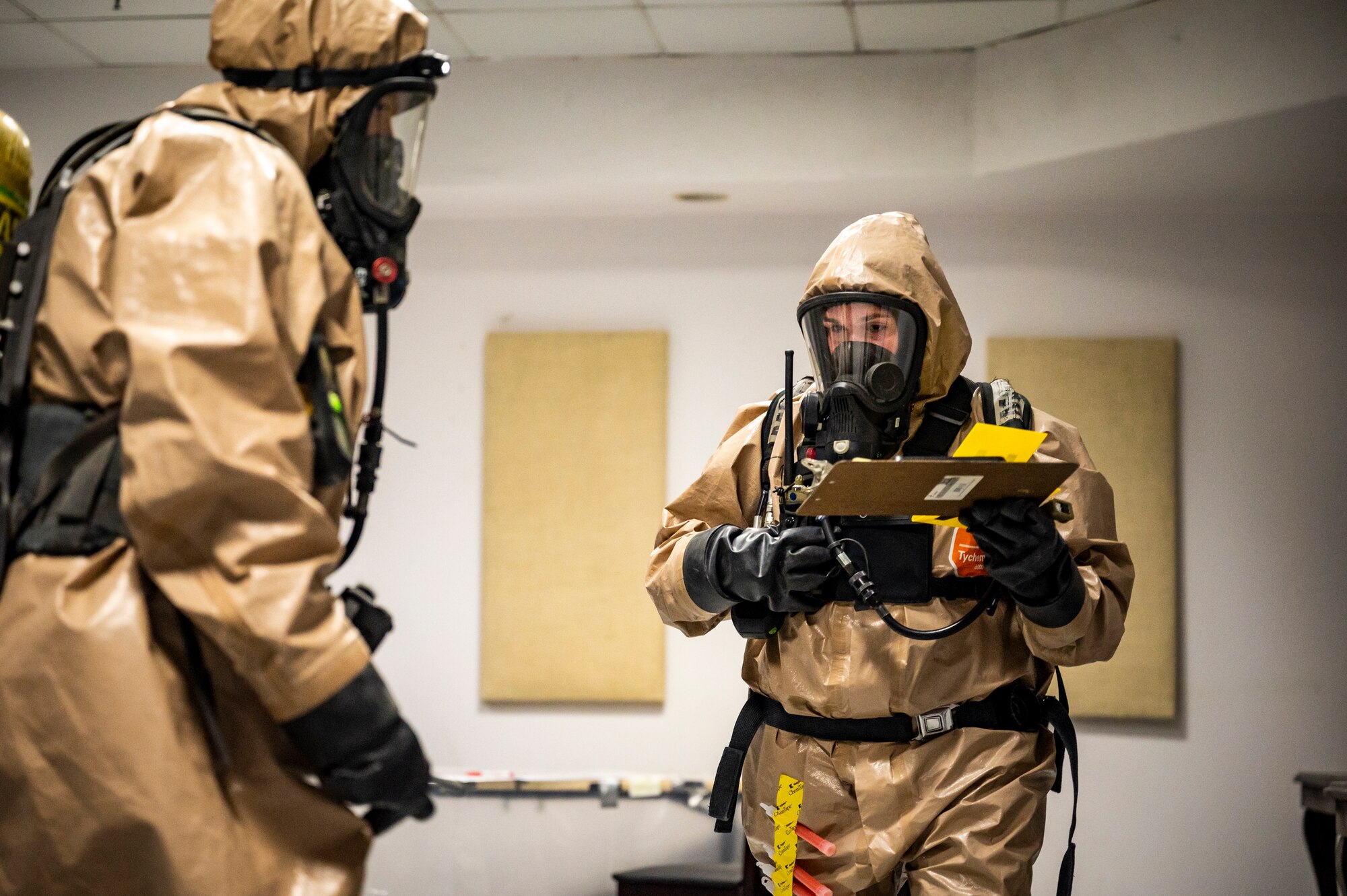 Military members in chemical gear uses a radio to talk to their team.