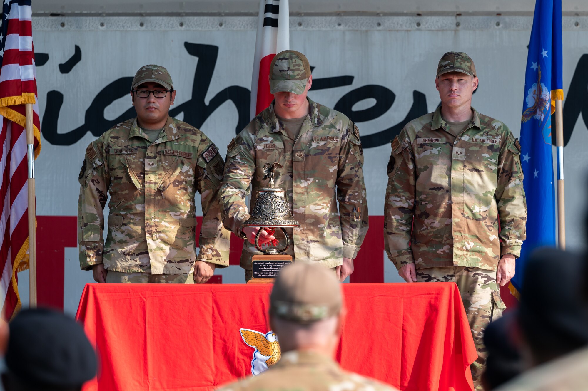 From left, Senior Airman Michael Craddock, Senior Airman Ryan Foley, and Senior Airman Bryce Shearer ing a bell during a 9/11 remembrance ceremony at Kunsan Air Base.