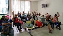 Family members in a waiting room wave to the camera.