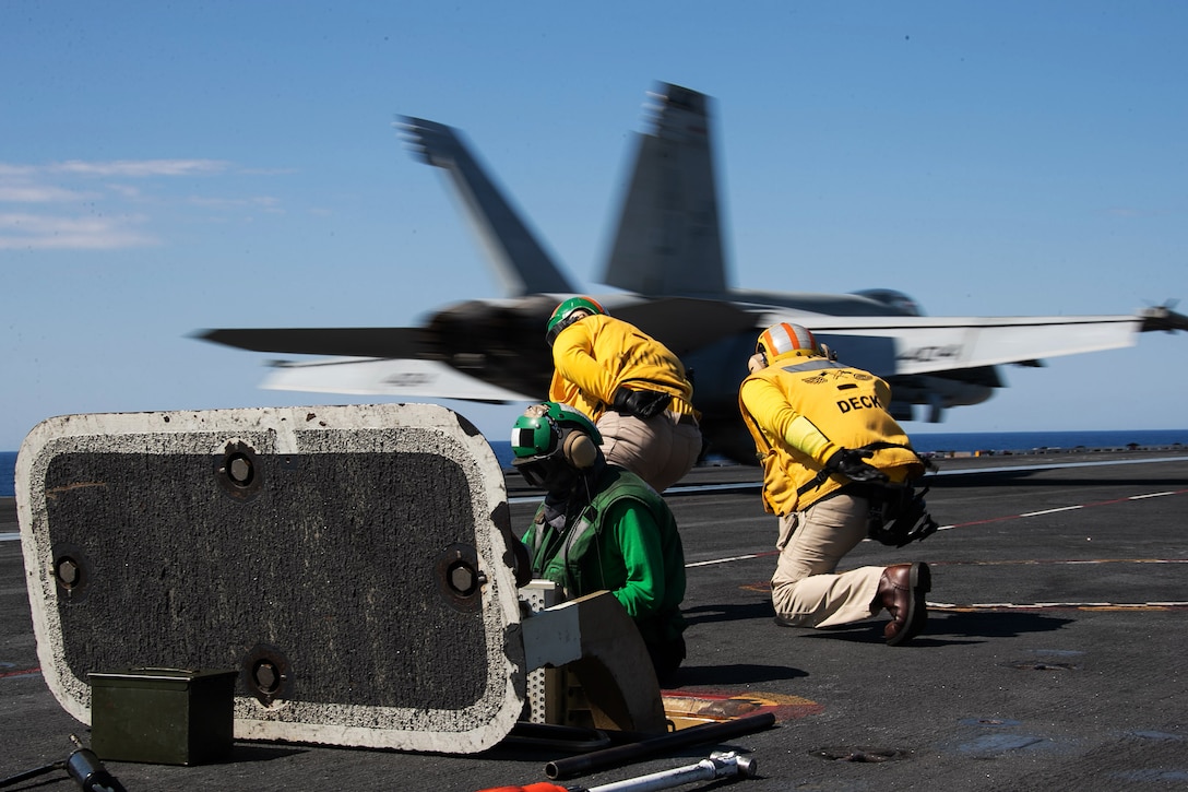 Sailors assist incoming planes by giving landing directions.