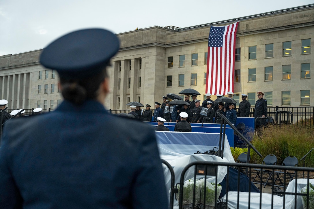 A service member in the foreground looks toward an American flag hanging on the side of the Pentagon.